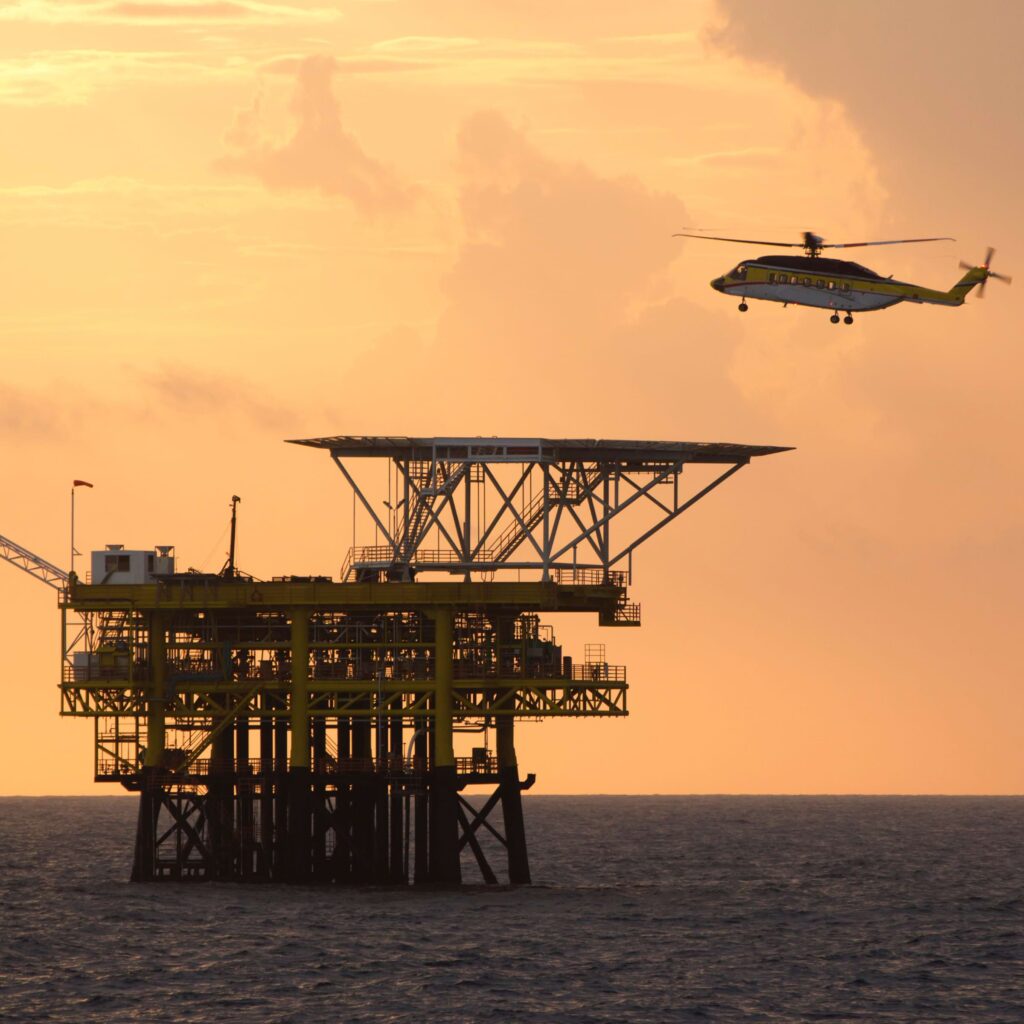 a helicopter flying over an oil platform in the ocean.