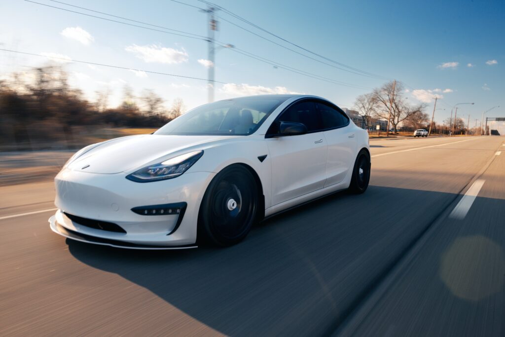 a white tesla model 3 driving down the road.